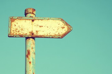 Rusty directional sign against a pale sky