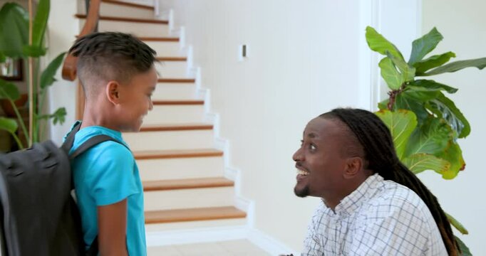 Happy black father talking to and high fiving with his multiracial son after he came back from schoo