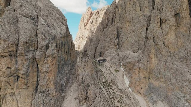 Panning drone shot of the remote Toni Demetz Hut perched high in the Dolomites, with sweeping views of rugged cliffs, alpine trails, and dramatic mountain scenery