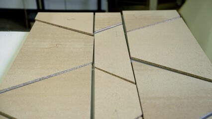 Skilled carpenter carefully aligning wooden triangular pieces on workshop table, constructing geometric wooden structure with precise craftsmanship and professional woodworking technique