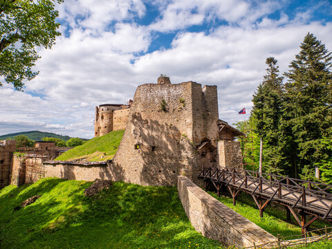 Ruins of Zborov Castle near Bardejov, Slovakia, with a wooden bridge and stone walls, surrounded by lush forest and blue sky.