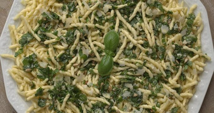 Ligurian cuisine: Trofie al Pesto. Trofie pasta with roughly chopped pesto on a plate. Flat lay, table spin.