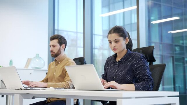 Portrait of smiling female manager sitting at desk at workplace in modern business office. Smiling professional woman working on computer and looking at camera. Successful businesswoman in workspace