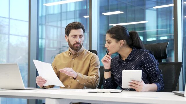 Professional business meeting between two financiers in modern office, discussing important documents with focus collaboration on work project. Colleagues consult about details, busy with paperwork