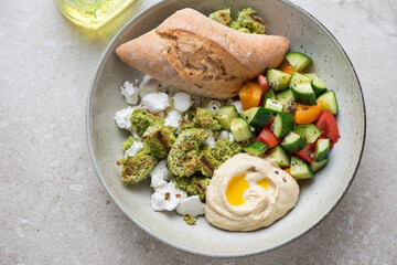 Plate with falafel, hummus, goat cheese and vegetable salad, horizontal shot on a beige stone background, high angle view