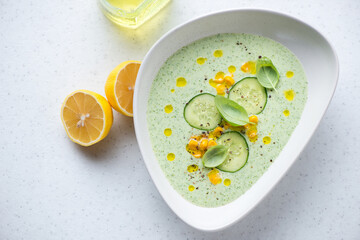 Chilled soup made of cucumber and topped with sweet corn, horizontal shot on a white stone background, top view