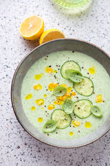 Plate of chilled cucumber and sweet corn soup on a light-grey granite background, vertical shot, elevated view
