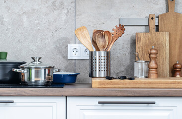 Kitchen countertop with utensils, pans on induction hob, bowls, cutting boards.