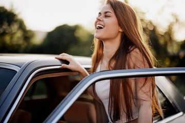 Happy young woman with long brown hair enjoying a sunny day by the car, wearing a casual outfit and...