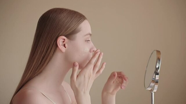 Young woman applying foundation or BB CC cream during her morning beauty routine. Light makeup for a natural look and skin enhancement. Gen Z female focusing on healthy glow and even skin tone.