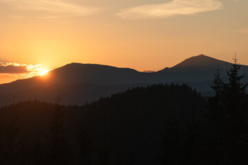 Sunset casts warm hues over mountains and forests in tranquil evening landscape. Hiking in Carpathian Mountains, Ukraine
