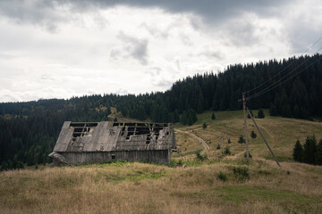 Old wooden barn stands alone in the mountains under cloudy skies with surrounding grass and forest. Hiking in Carpathian Mountains, Ukraine