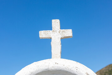 White cross standing on whitewashed dome against blue sky