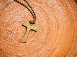 Tau cross pendant resting on a terracotta surface