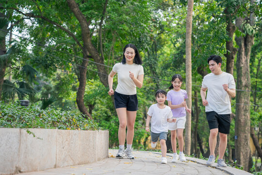 Family enjoying a morning jog through a lush park surrounded by green trees and nature