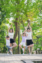 Fototapeta premium Family practicing yoga poses together in a green park during a sunny day