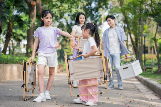 Children and adults enjoy a sunny day in the park carrying folding chairs while sharing smiles and excitement