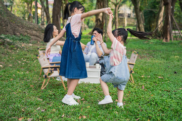 Fototapeta premium Children dancing joyfully in a park while adults enjoy a picnic in a lush green setting during a sunny day