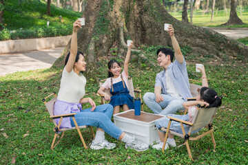 Group of friends enjoying a picnic in a park while raising cups in celebration during a sunny afternoon gathering