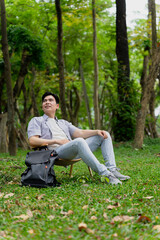 Obraz premium Man relaxing on a chair in a green park surrounded by trees during daylight