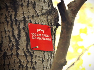 red hiking trail sign on tree trunk, 100 km trail around Vilnius marker in forest