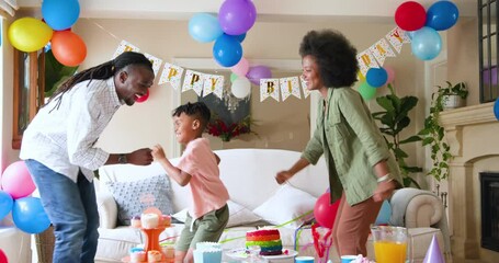 Happy black couple and their multiracial son dancing and smiling, celebrating boy's birthday at home