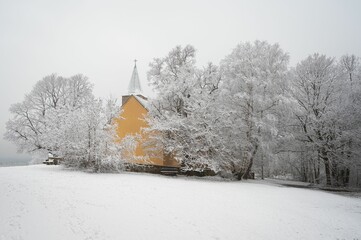 a church with a steeple covered in snow and trees in the background