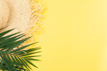Vacation travel planning simple theme of straw hat and palm leaves on uniform yellow background flat lay with copy-space