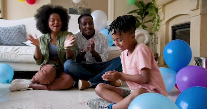 Happy black couple and their multiracial son throwing party streamers smiling, celebrating boy's bir