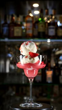 Scoops of white ice cream in strawberry sauce in a glass spinning on a bar counter