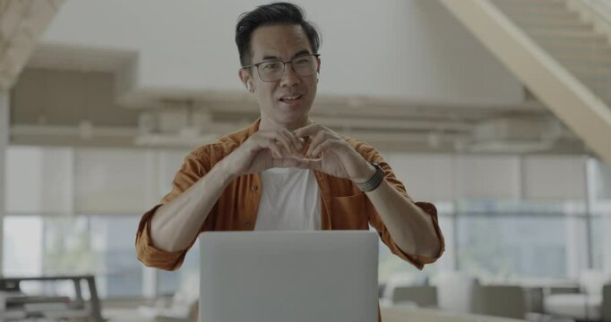 Senior Asian businessman wearing headset celebrates success during online meeting in modern co-working space. Remote work and business communication concept.