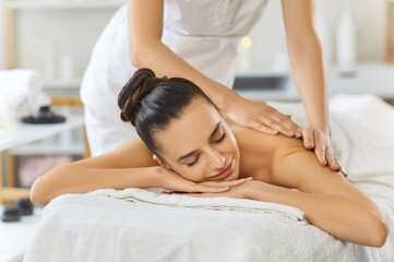 Pleased brunette woman enjoying healing massage in modern spa salon, lying on stomach on couch,...