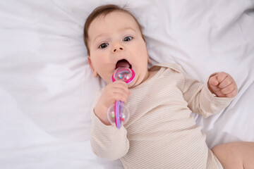 Cute little baby with rattle toy on bed at home, above view