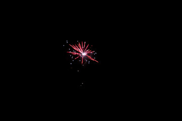A photograph of a single, bright firework spark or burst against a stark black sky, capturing a moment of fleeting light.