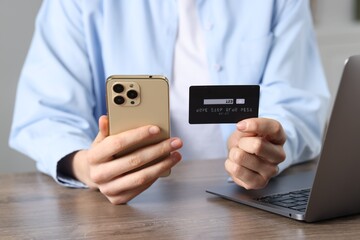 Woman with credit card, smartphone and laptop paying online at wooden table, closeup