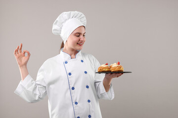 Confectioner in uniform holding delicious profiteroles and showing ok gesture on light grey...