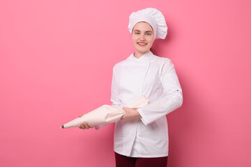 Confectioner in uniform holding pastry bag on pink background