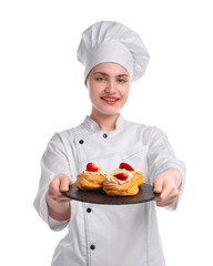 Happy confectioner in uniform holding delicious profiteroles with strawberries on white background
