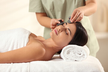 Young woman receiving facial massage with spa stones in salon