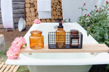 Outdoor bathtub with soap bottle, candle, and pink flowers for a luxurious self-care experience in nature. Relaxation and spa concept for escape and wellness.