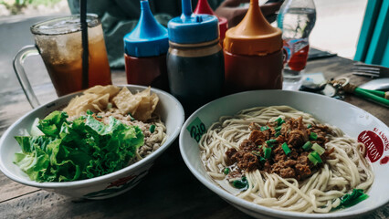 A full portion of cwie mie and chicken noodles with iced tea and some sauces.