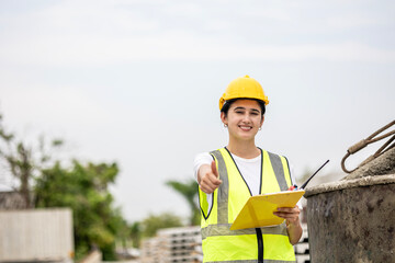 Female worker or engineer wearing safety gear, a yellow hard hat and vest. Construction worker is...
