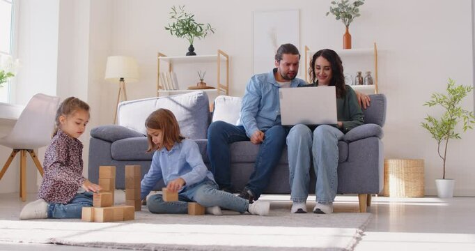 Happy family rest at home, children sister and brother playing, parents relaxing at home on sofa with laptop, little boy, girl having fun, friendship, family leisure time in cozy modern living room 