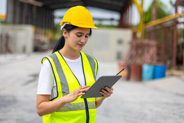 Female worker or engineer wearing safety gear, a yellow hard hat and vest. Construction worker is...