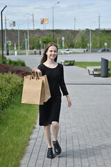 Woman walking with shopping bags outside on a sunny day in casual black dress.