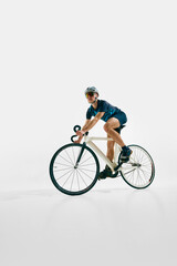 Obraz premium Side view low angle image of focused man, professional cyclist in full gear, riding bike, training isolated on white background. Concept of sport, competition, active lifestyle, endurance