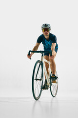 Full-length front view image of young man in full gear, cyclist in helmet and goggle riding bicycle isolated on white background. Concept of sport, competition, active lifestyle, endurance