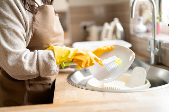 Washing dishes in a modern kitchen with yellow gloves during a sunny afternoon