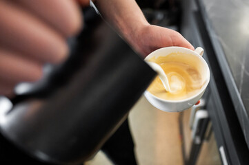 A barista skillfully pours steamed milk into a cup of espresso, creating a beautiful latte art...