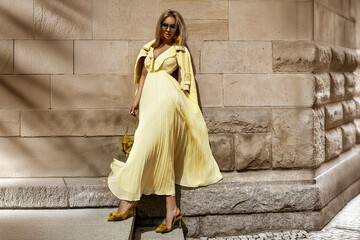 Summer fashion model in flowing yellow maxi dress poses in the city on a sunny summer day.